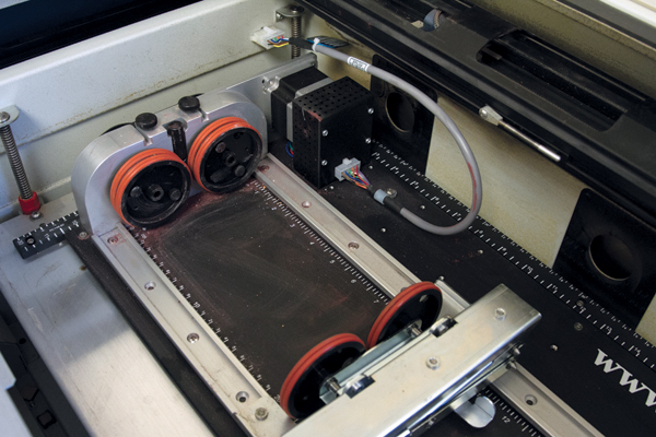  6 Detail image of the Zing 24 Laser Rotary Attachment inside of the laser etcher. The rotary attachment allows for printing onto a round surface.