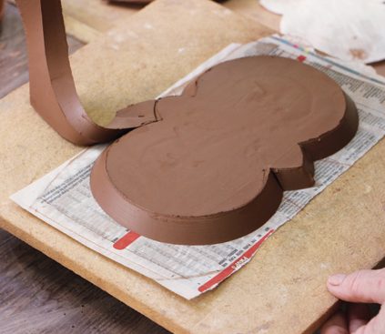 3 Remove the extra clay and use a rib to compress the angled edge. Place a board on top and flip the base over.