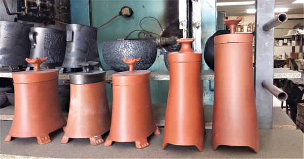 13 Front row: lidded jars in process, ready for engobe patterns to be added. Back row: Finished pots on a shelf in front of the kiln.