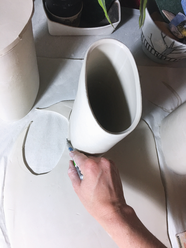 1 Throw a straight-sided, bottomless cylinder and alter it into an oval shape. Place the cylinder onto a ¼-inch thick slab, and use it as a guide to cut out the bottom.