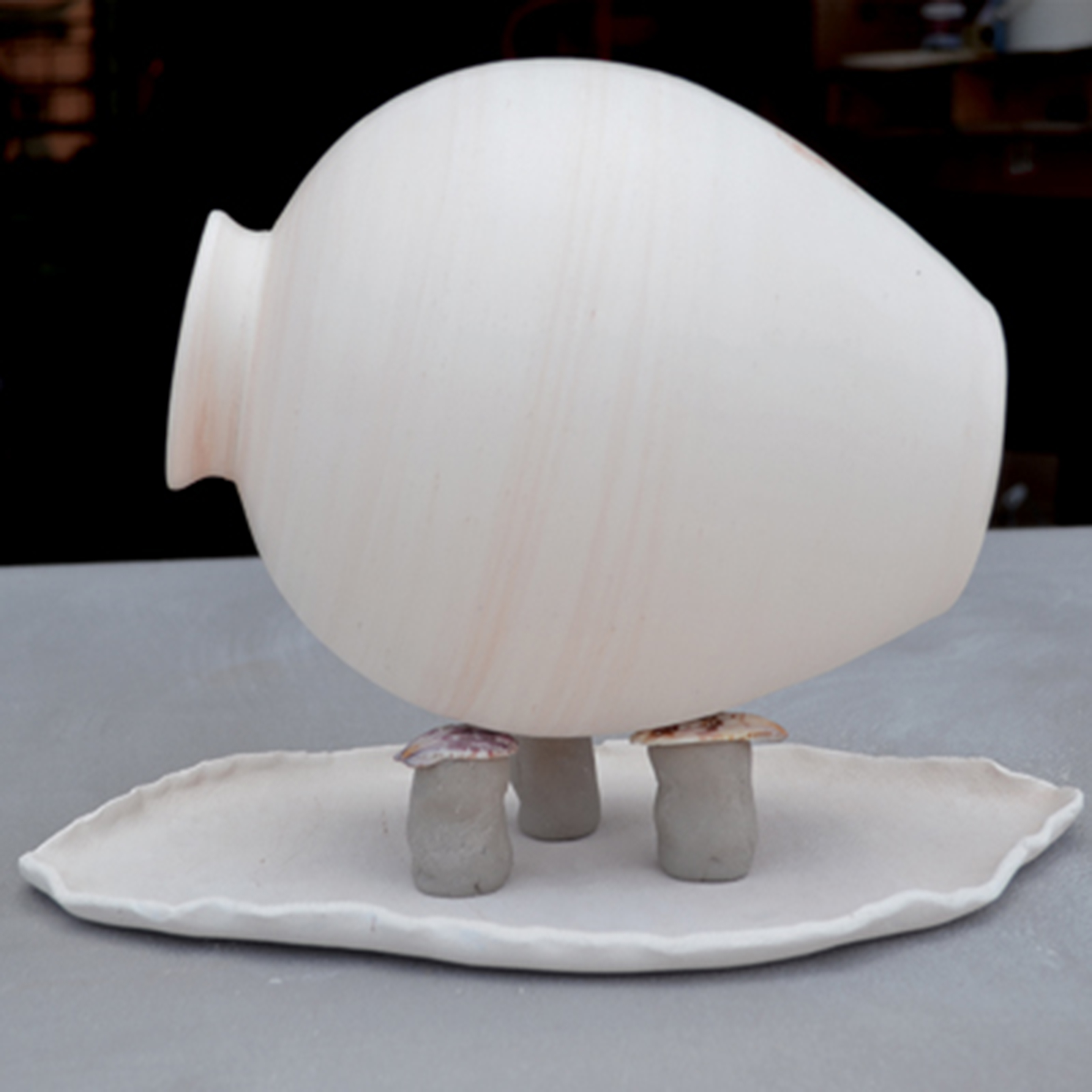 5 Place three cylindrical wads on your drip tray in a triangle. Top the wads with sea shells. Place a glazed pot on its side on top of the sea shells.