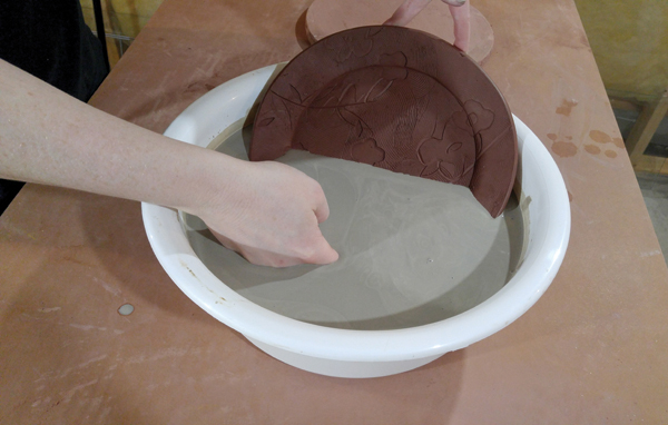 6 Holding the plate with two fingers on either side, then dipping it into white slip.