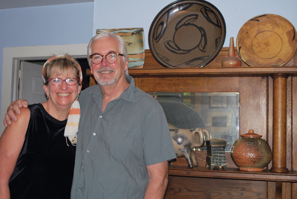 2 Image of Suze Lindsay and Kent McLaughlin in front of their living room mantle. Top shelf: platters (left to right): Suze Lindsay, Scott Goldberg, Rock Creek Pottery (Will Ruggles and Douglass Rankin); Jan McKeachie Johnston’s vase. Bottom shelf: Earl Robbins’ animal vessel, Michael Simon’s box, Kent McLaughlin’s shino jar. 