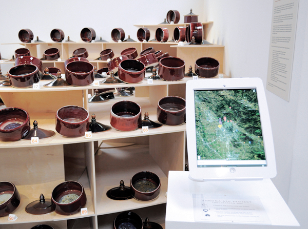 Gregory Roberts’ Sonoma Ash Project installed at the Museum of Sonoma County, California (wood display by 180 Studios, Santa Rosa, CA), 2018. The project included 130 porcelain vessels with lids that incorporated ash donated by residents from homes lost in the Tubbs Fire. In the foreground, a tablet displays an area affected by the fire, with markers indicating the locations of participants’ former homes. Courtesy of the Museum of Sonoma County.