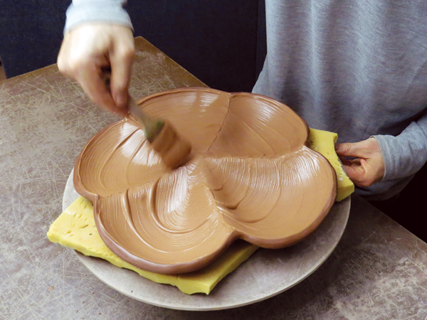 9 Flip the platter over onto the foam to prevent marring the carving on the bottom and apply thick, textured slip to the interior.