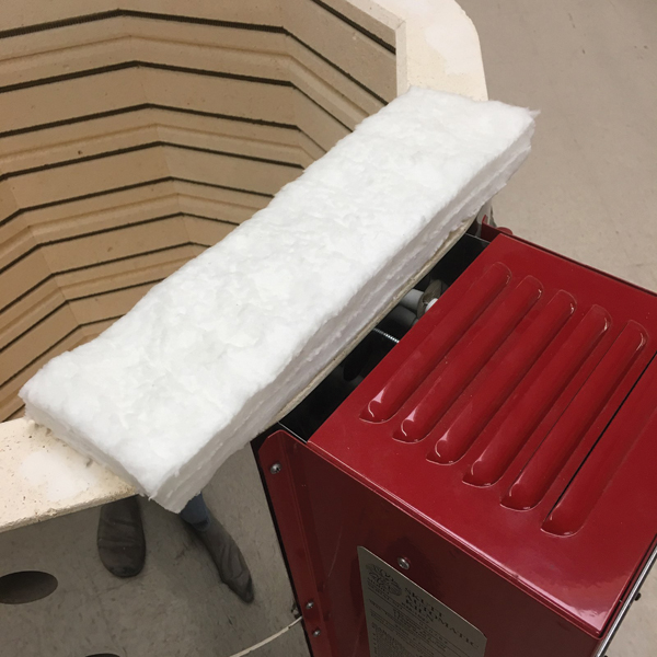 Proper placement of the ceramic fiber blanket lid prop on an electric kiln shields the control box from excessive heat while venting combustion gases.