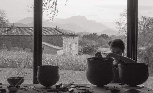 7 Enjalbert adding a coil to a pot, with two other pots in progress on the table and the countryside and slopes of the Pyrenees visible through the studio windows in the background. Photo: Jérémie Logeay.