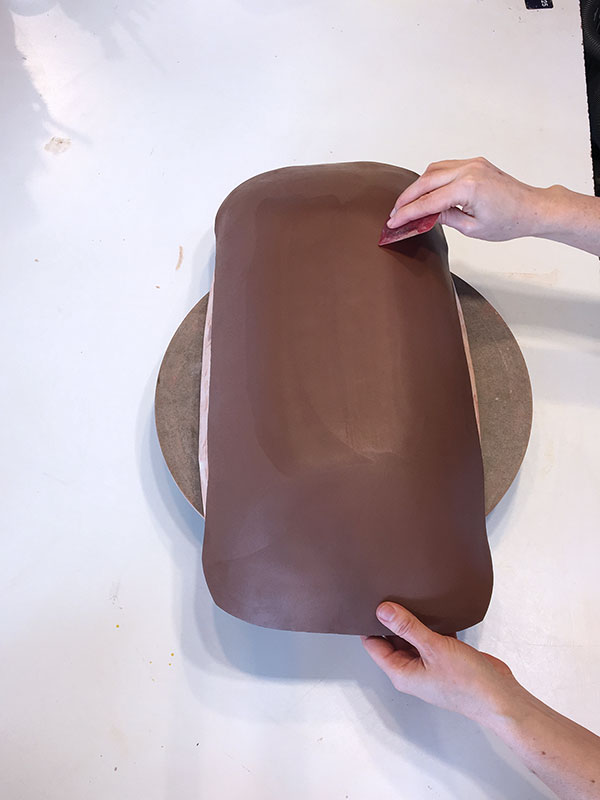 2 Smooth and compress a slab of clay onto the bisque mold with a rubber rib. 