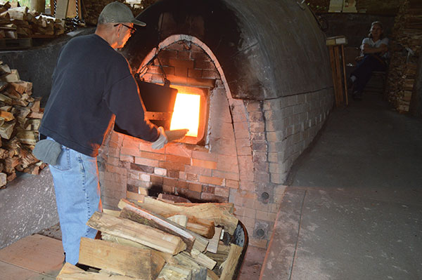 7 Rowland feeding wood into his glowing anagama kiln during a firing held at the end of 2019. Photo: Nancee Long.