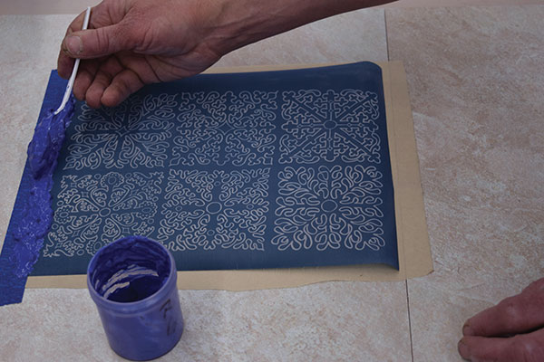 5 Tape the dry stencil onto a flat surface, slip a piece of paper under it, and spoon a line of thickened underglaze along the top.