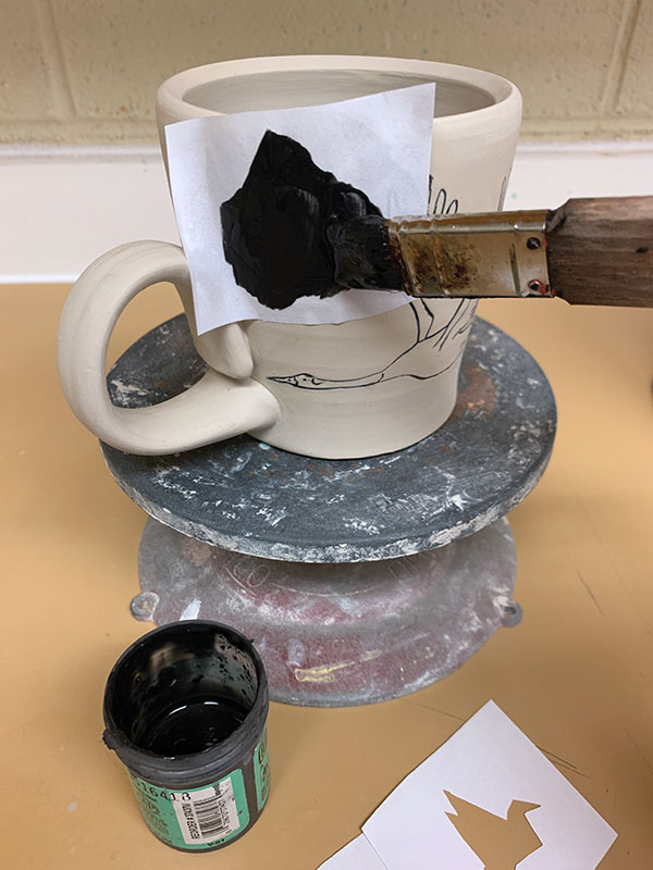 5 Paint underglaze into a paper stencil placed on the mug’s surface. 