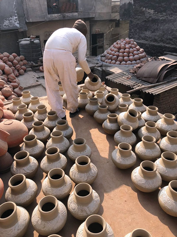 13 Water jars that are ready to be fired are brought out to the kiln area in the courtyard. The kiln is in the background, with a load of fired pots stacked in a dome at the top, shown with the protective metal covering and insulating shards removed.