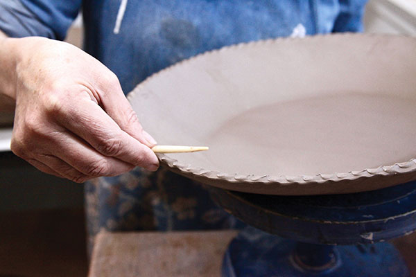 1 After making, the slab dishes are dried evenly to a leather-hard stage then the rim is fluted using a wooden tool prior to applying any slip to the surface.