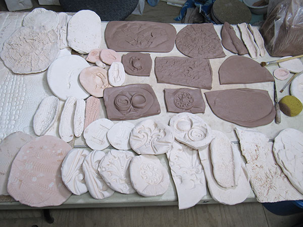 6 On-site molds and clay pressings including a crushed beer can, ironwork, sidewalk cracks, corn cobs, and woodwork.