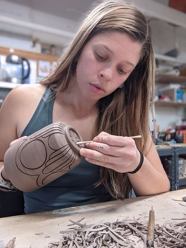 3 Erika Novak carving a design on the bottom of a leather-hard tumbler.