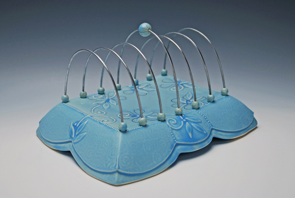 3 Kristen Kieffer’s toast rack, drape-molded and altered porcelain, carved, slip-sponged, underglaze, slip trailed, and mishima decoration, multiple glazes, oxidation fired to cone 7, steel wire, 2014.
