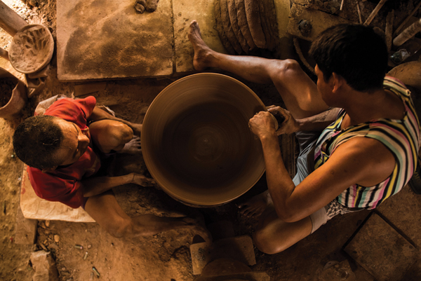 1 Manual pottery wheel being operated by two potters. One keeps the wheel turning while the other throws and coil builds the pot.