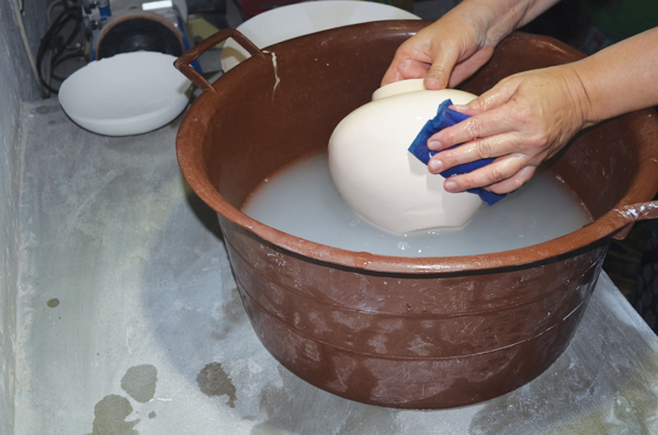 Final polishing of the bisque-fired pot to remove any texture and achieve a smooth surface.
