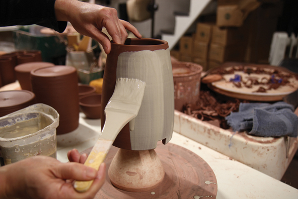 7 Prop the canister right-side up on a narrow chuck, then brush white slip onto the canister’s body.