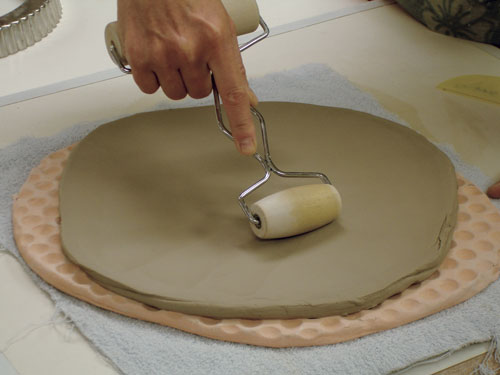 Place the slab onto the first texture tool, gently roll from the center towards the edge in a radial pattern, pushing down just enough to press the clay into the texture, but not so hard that you move the clay and thin the slab.