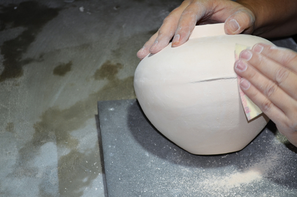 Wet sanding the bisque-fired vase to remove seam lines from the mold.
