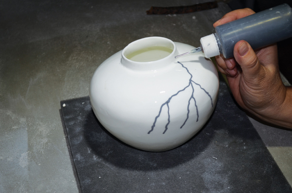 Applying an underglaze tree-branch pattern to the glaze-fired piece using a slip-trailing bottle.