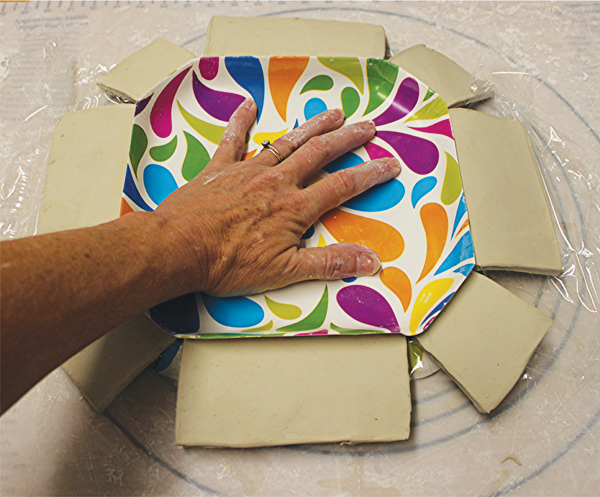 6 Use the rimless paper plate to push the clay gently into the slump mold.