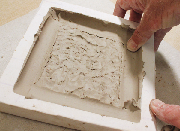8 Press a thin pancake of clay into the mold. Work from the center out to the top and bottom of the tile.